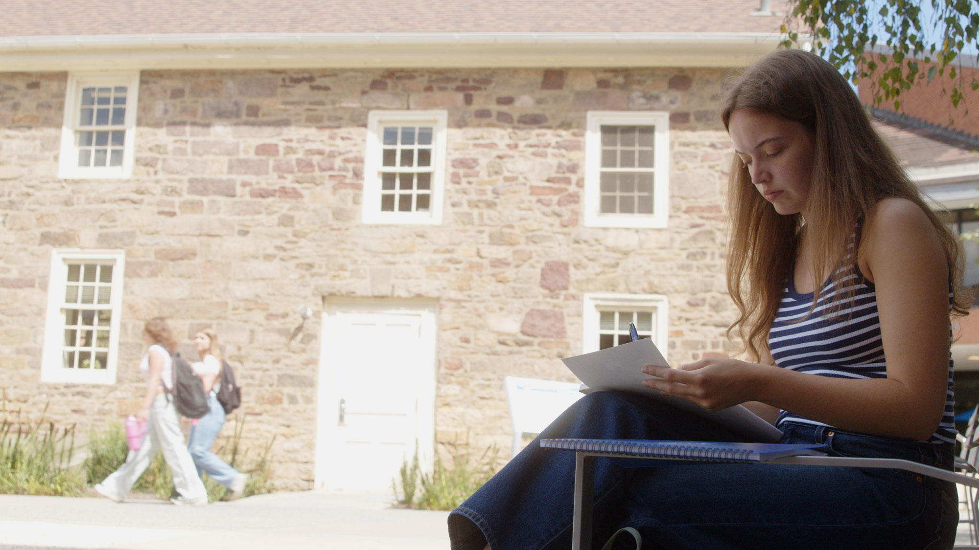 Young woman writing in a notebook outdoors in front of Cooper Homestead.
