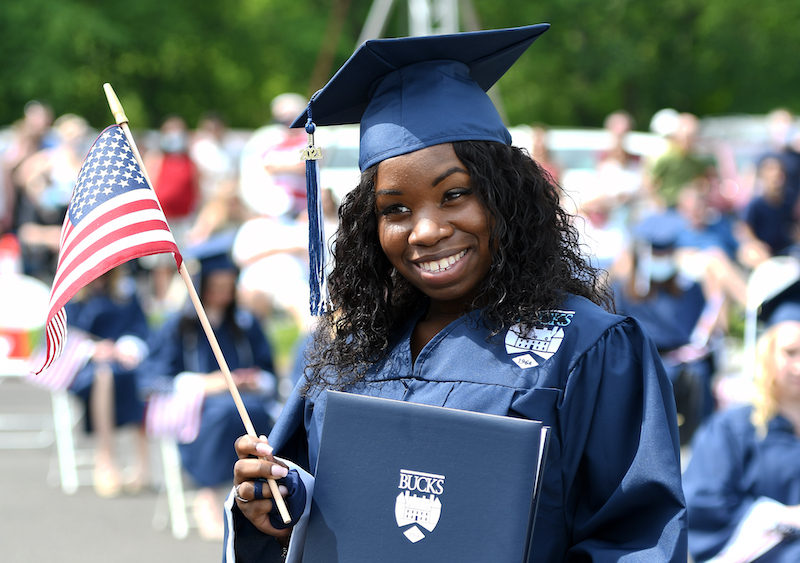 girl in cap and gown holding diploma and flag