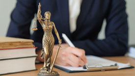 Scales of Justice bronze statue sits on desk with person writing on notepad in background