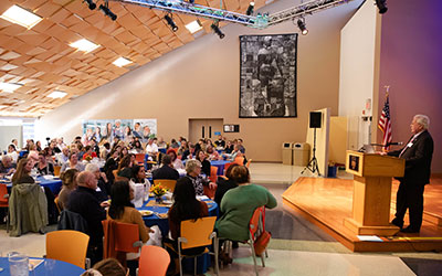 Speaker addressing a seated audience at a formal indoor event.