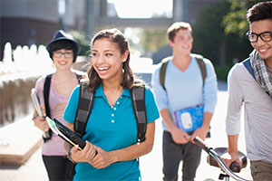 Young female walking in group of peers holding books wearing backpack