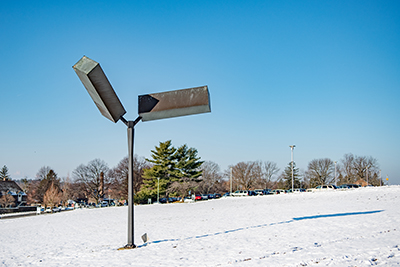 Steel sculpture with two suspended rectangles with blue sky in background and snow on the ground