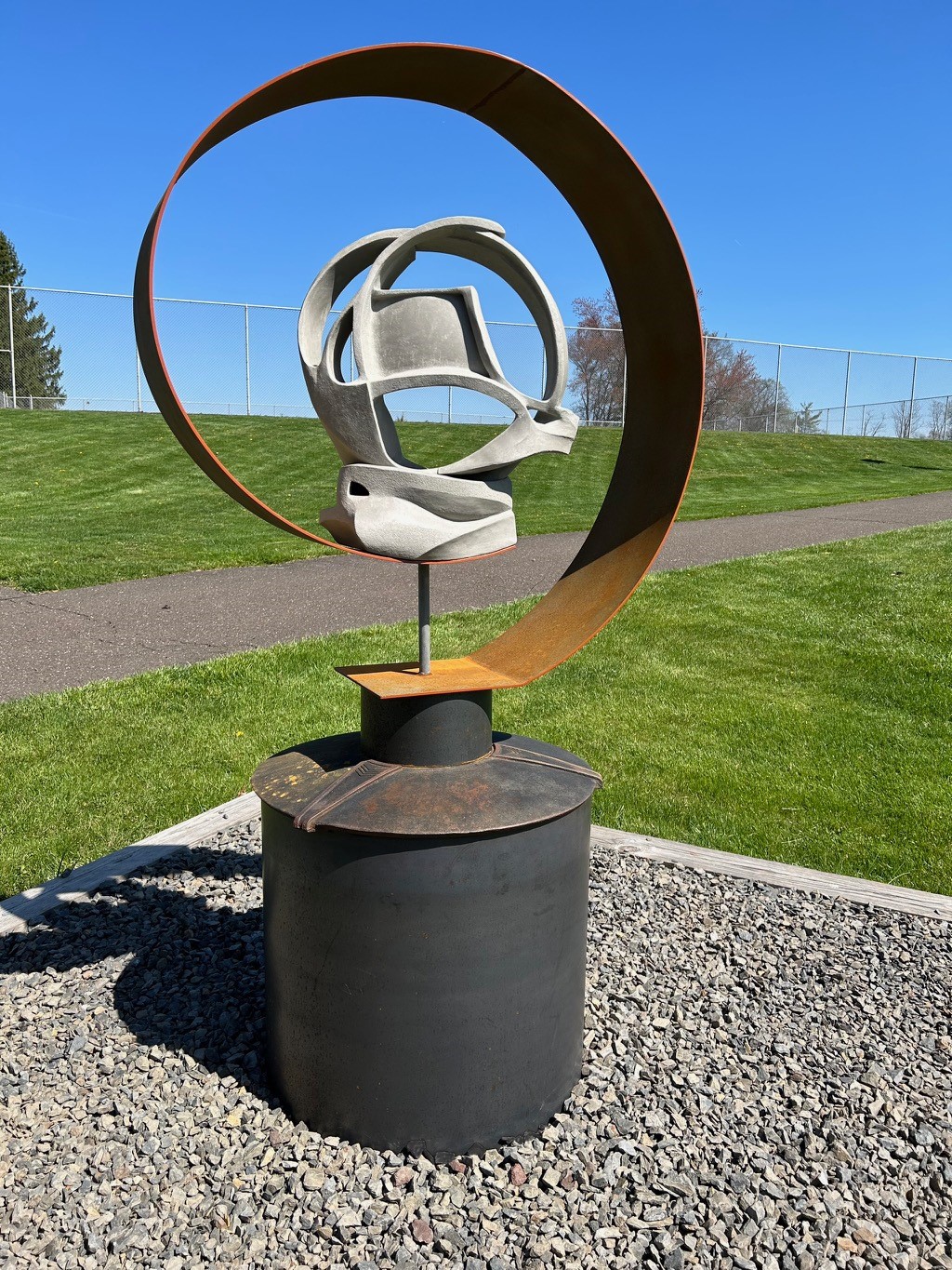 round steel and abstract ceramic sculpture mounted to steel base installed outdoors near tennis courts