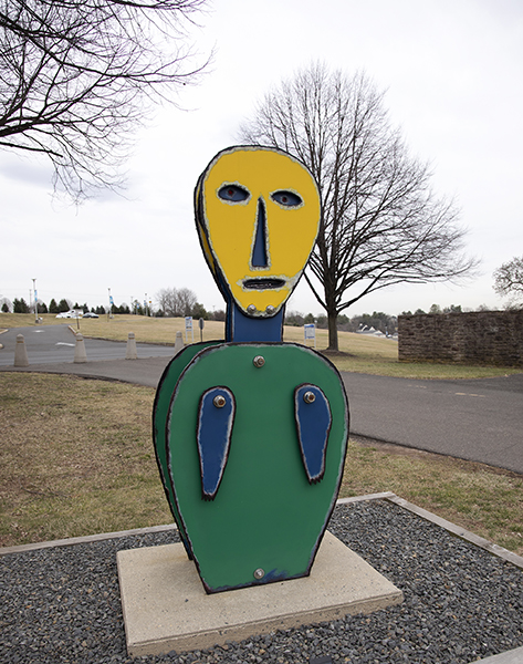 sculpture of an abstract figure with yellow head, green body and blue arms
