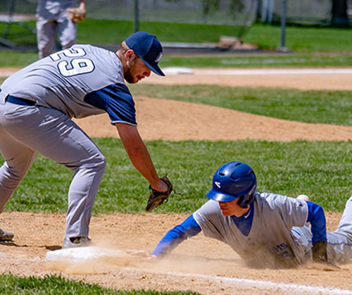 A baseball player slides into base, dirt flying as he reaches for the bag with his glove outstretched.