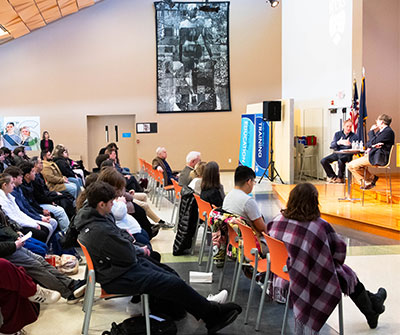 A large crowd of people seated in chairs, filling a spacious room.
