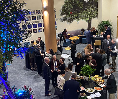 Several individuals stand around tables in the atrium, chatting and interacting with one another.