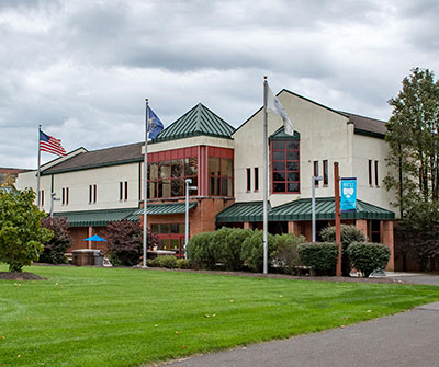 Gateway Conference Center, a two-story building with white stucco walls, green metal roofs, and flags flying out front, situated behind a grassy lawn.
