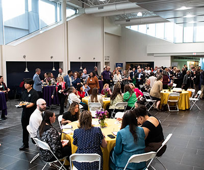 A large group of people seated at tables in a spacious room, engaged in conversation and activities.
