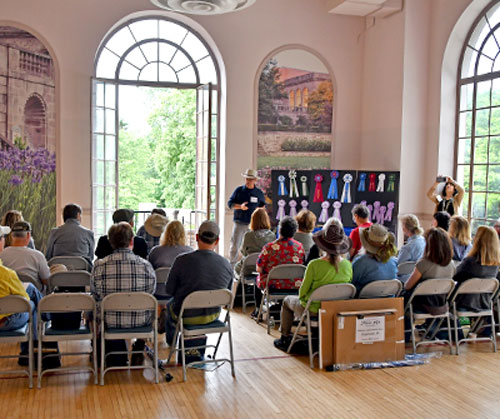 A spacious room with attendees sitting in chairs, and a man presenting at the front of the group.