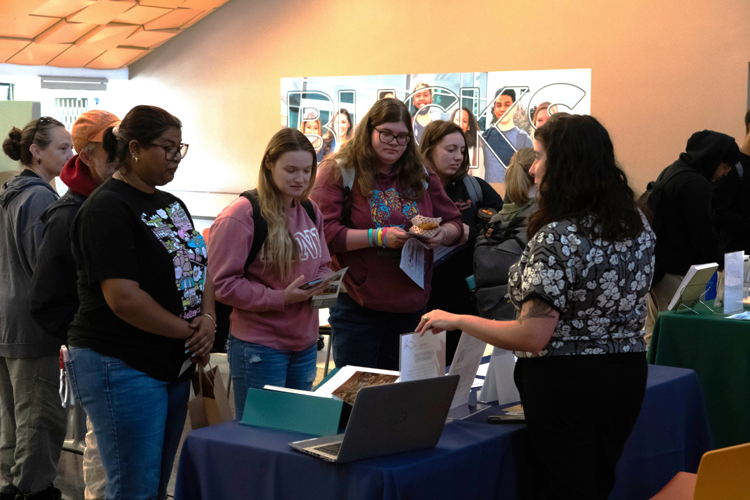 students talking to a staff member standing in front of a table