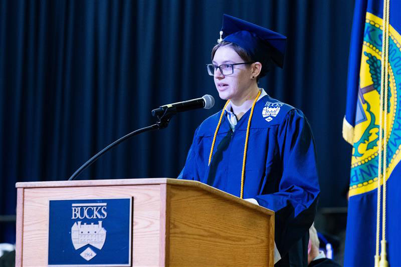 Sierra Kunigis, student speaker, in blue cap and gown speaks at a podium with 