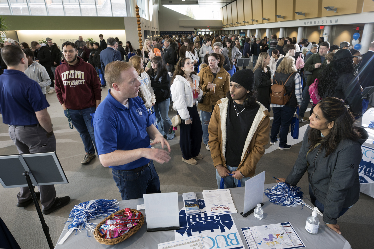A crowded open house with visitors engaging with a representative at an info table.