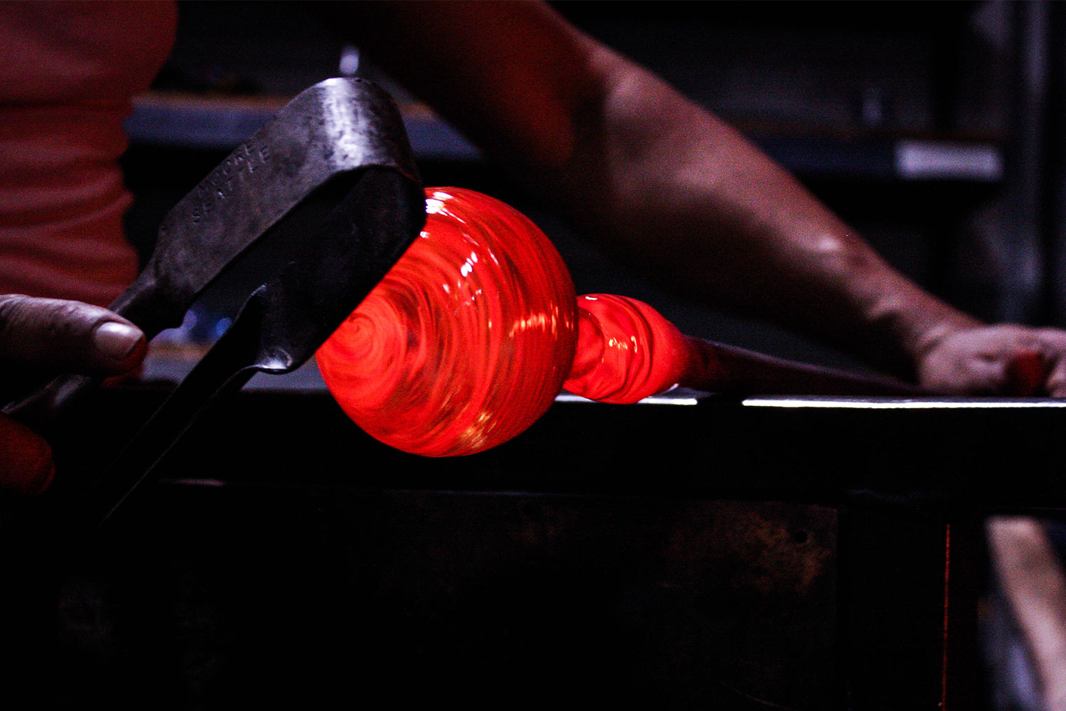 Close-up of glassblowing with a glowing red orb being shaped.