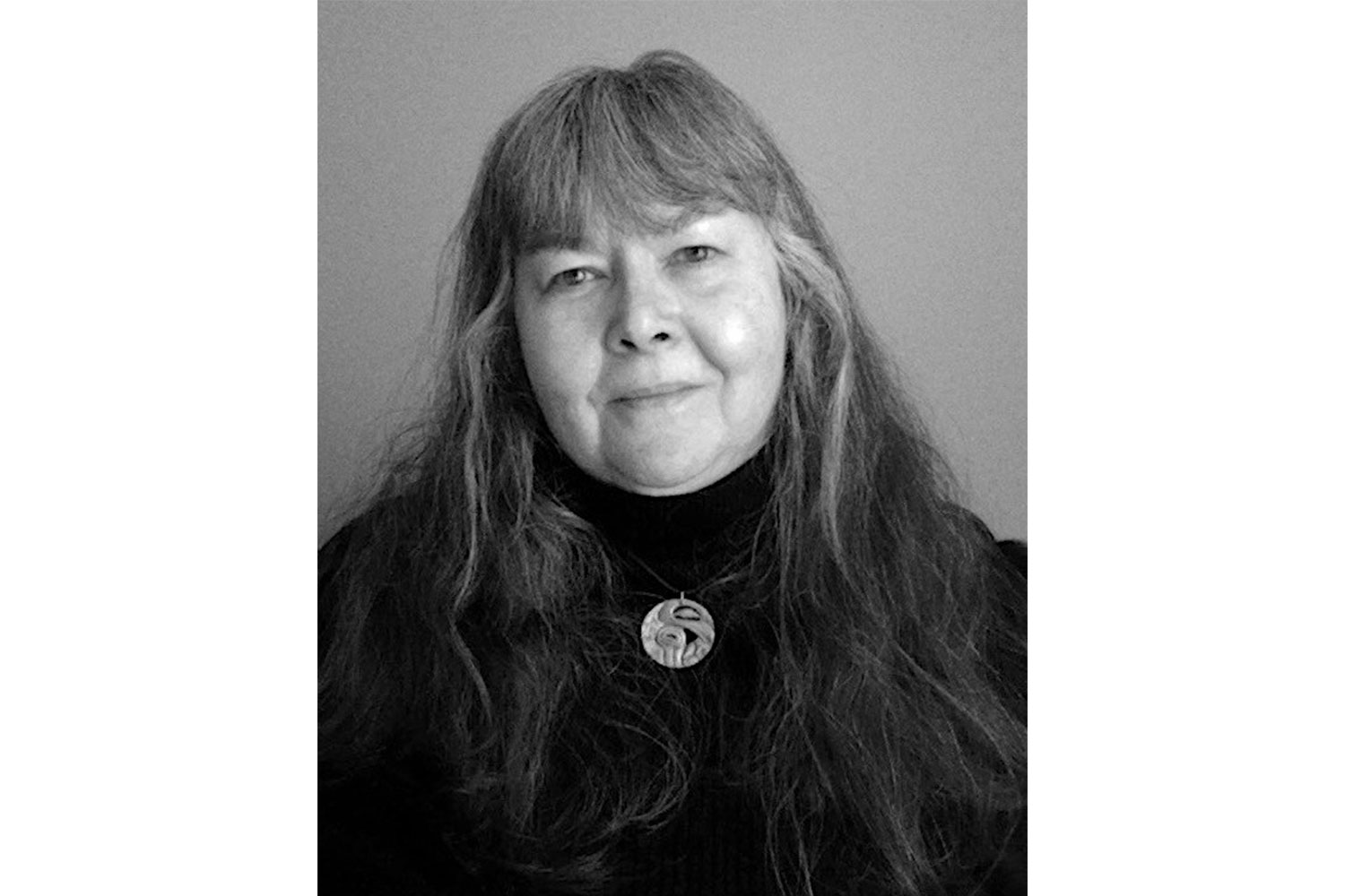 Black-and-white portrait of Lynda Gene Rymond with long wavy hair, wearing a dark high-neck top and round pendant necklace.