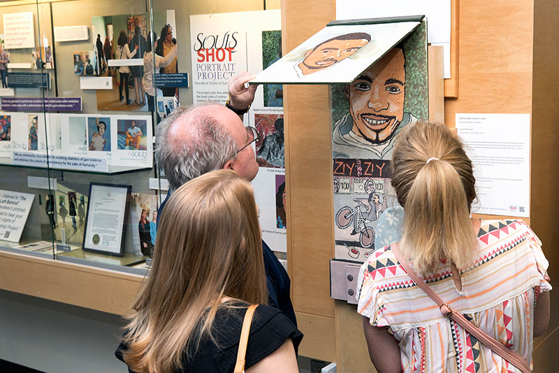 Visitors to the Gallery at Lower Bucks Campus examine an interactive display that tells the story of a young man lost to gun violence as part of the “Souls Shot Portrait Project”