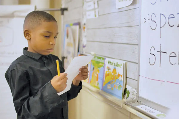 African American boy reading from paper in classroom