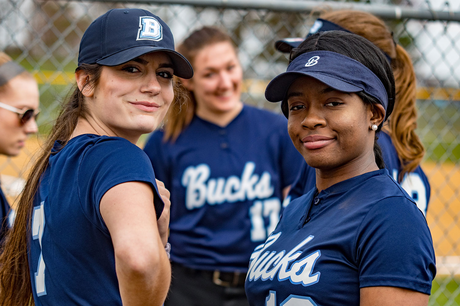 Two female softball players turned towards the camera smirking