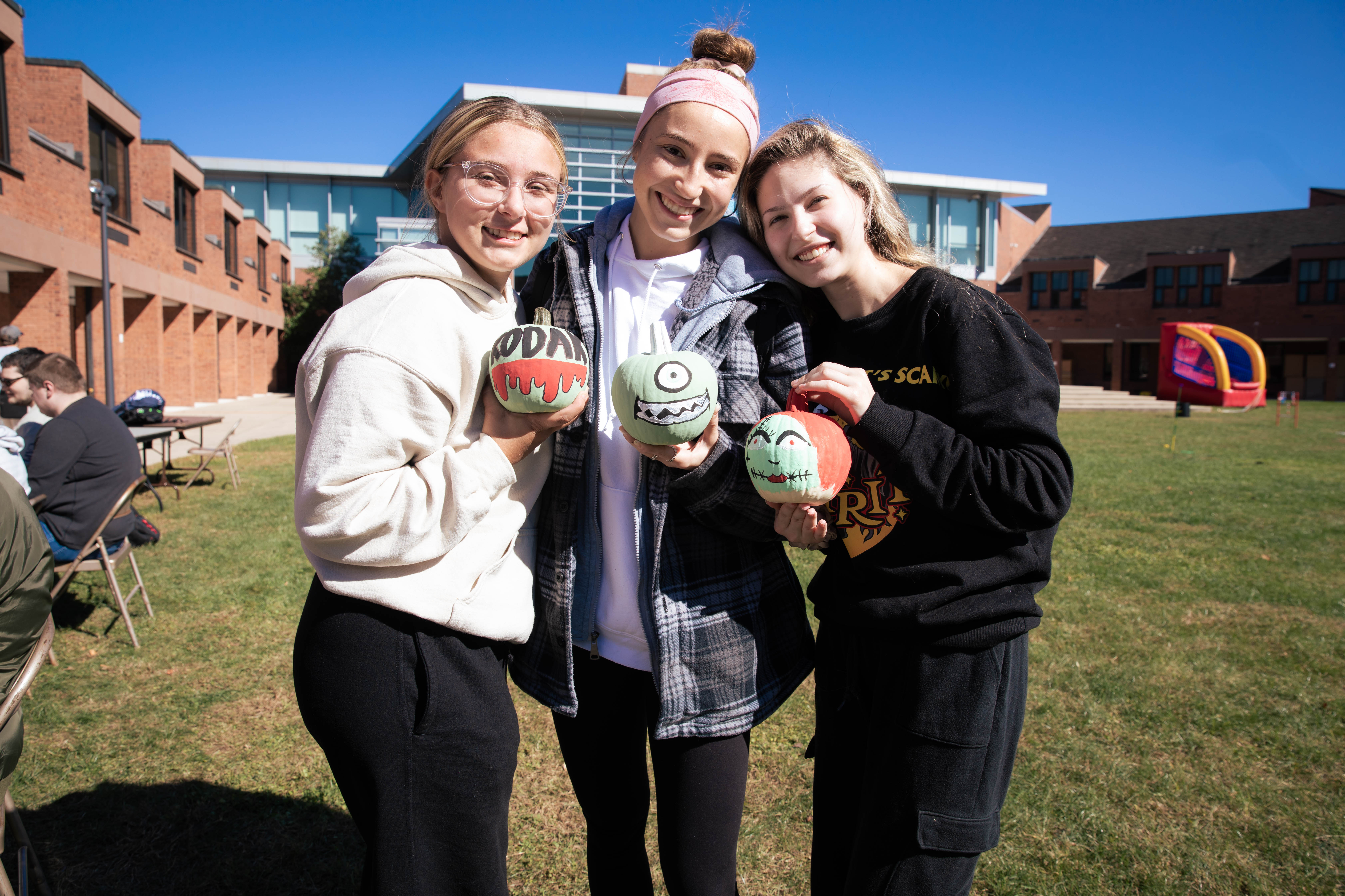 Three students holding pumpkins 