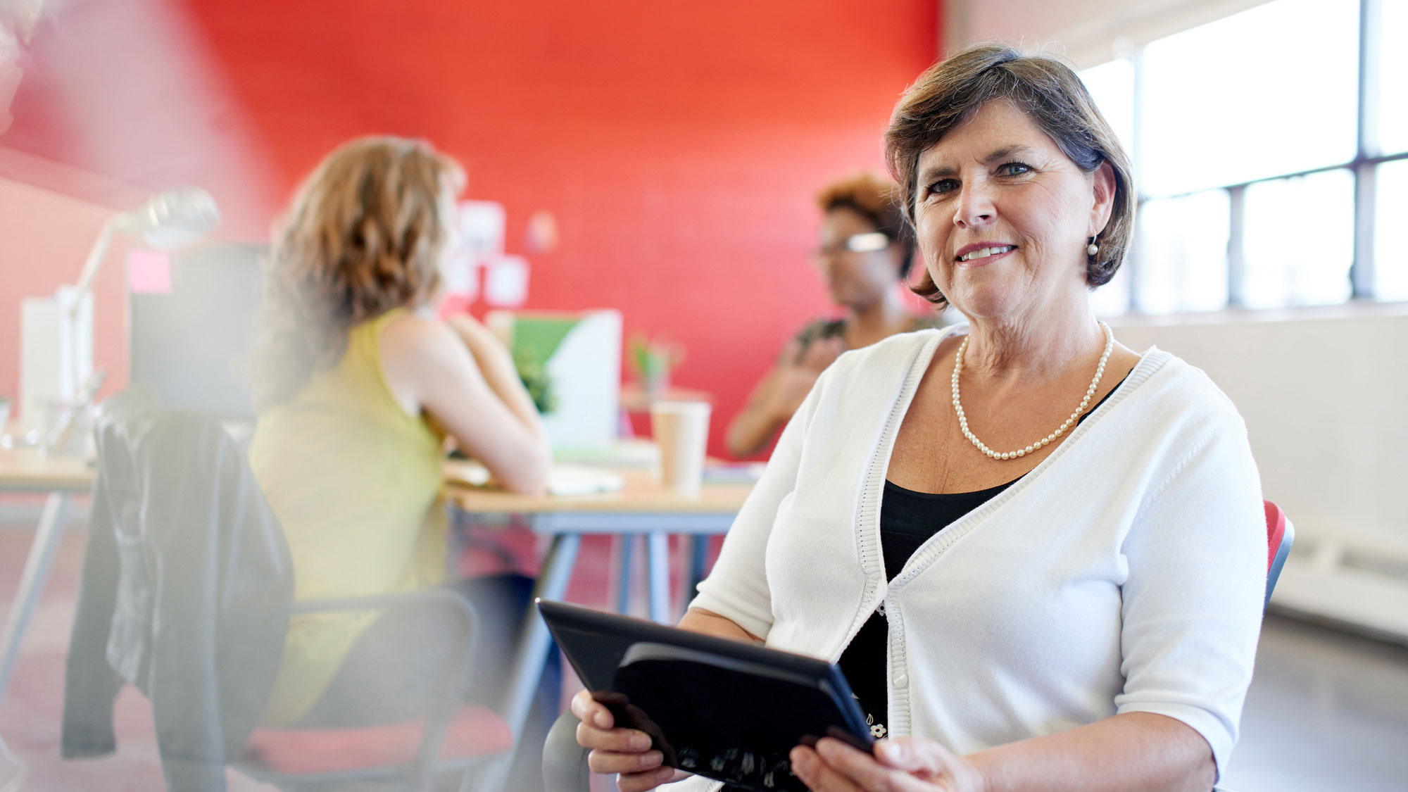 Mature business woman using technology in a bright office with the team in the background