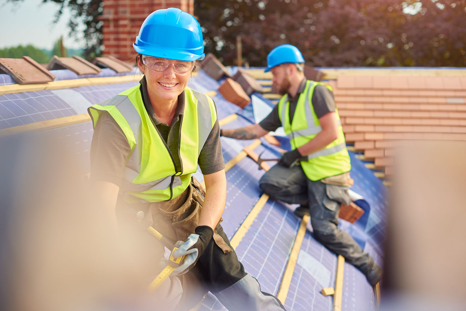 A female roofer nails on the roof tiles with her colleague
