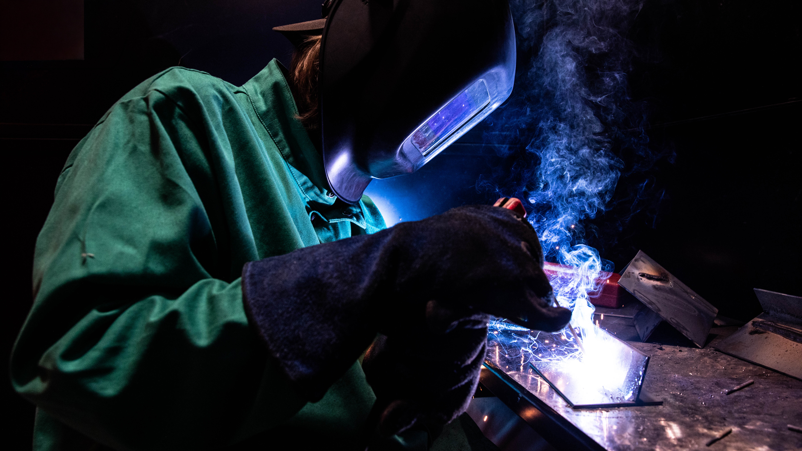 Bucks metalwork student using a welding torch on metal, with sparks and smoke visible.